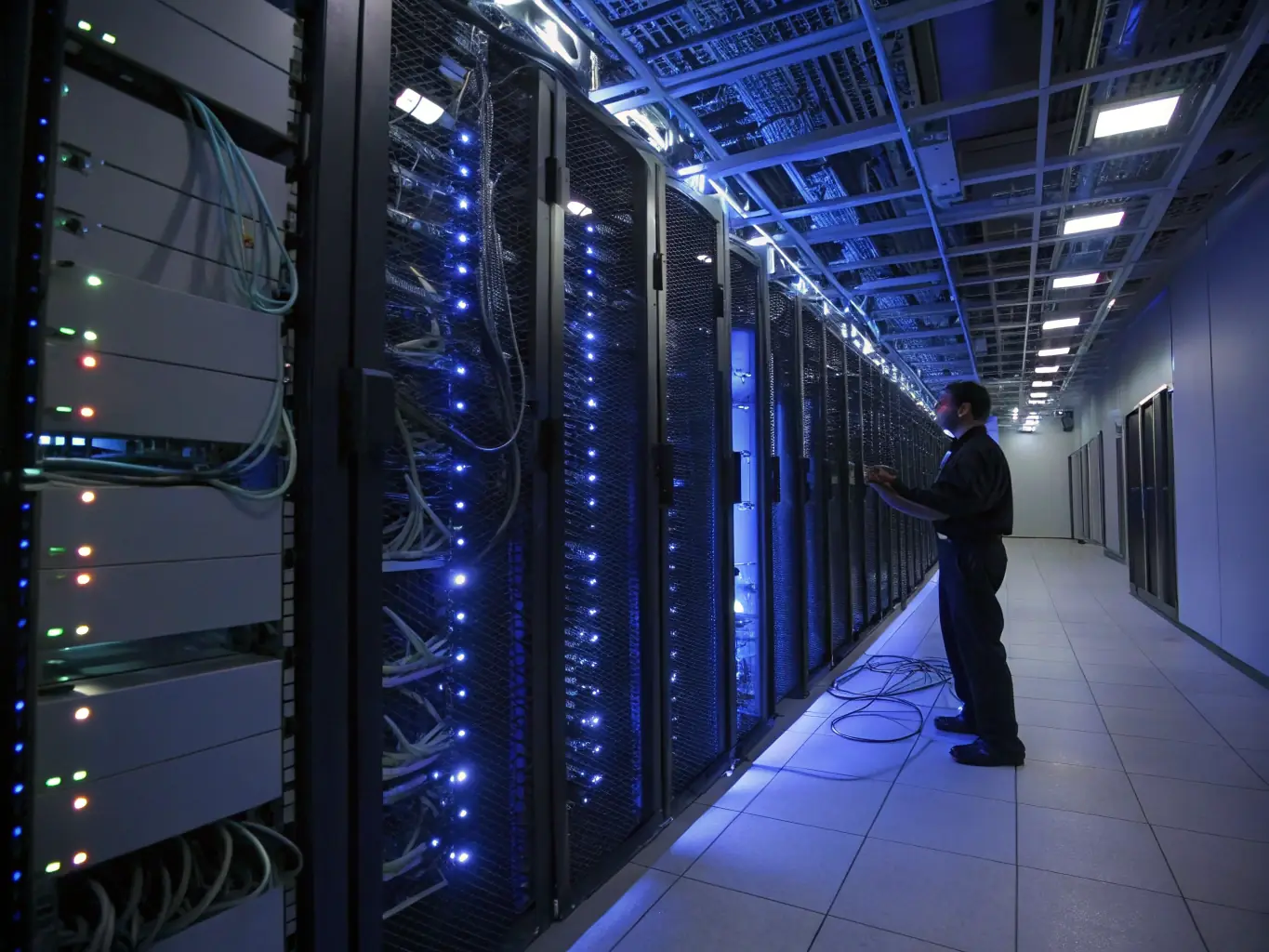 A data center with rows of servers and technicians working on fiber optic connections, highlighting the importance of high-speed data transfer.